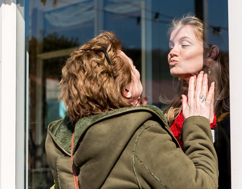Moeder en dochter geven elkaar kus door raam